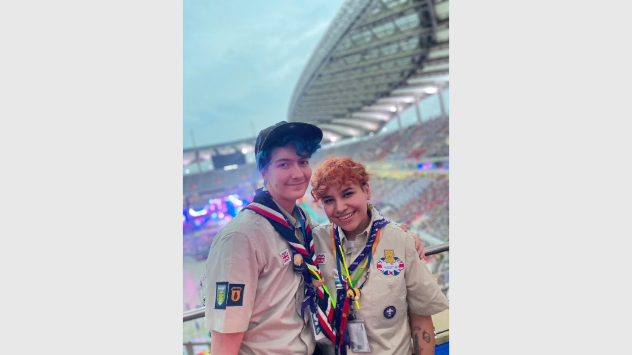 The image shows Jackson on the left and Astro on the right stood next to each other and smiling at the camera. They're both in Scouts uniform and they're stood in a stadium which you can see behind them.