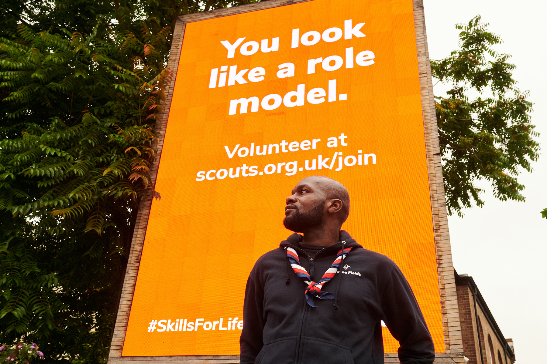 Dwayne Fields, wearing a black jacket and necker, stands in front of a sign saying 'You look like a role model'.