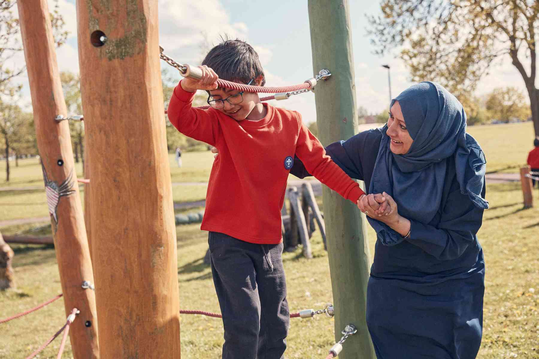 A Squirrel, wearing a red jumper, walks on a climbing frame while holding the hand of a leader.