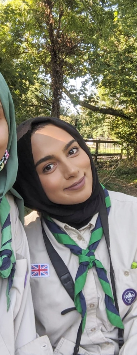 Humaairah Jama smiles at the camera wearing a black hijab, beige Scouts shirt and green and blue stripy scarf