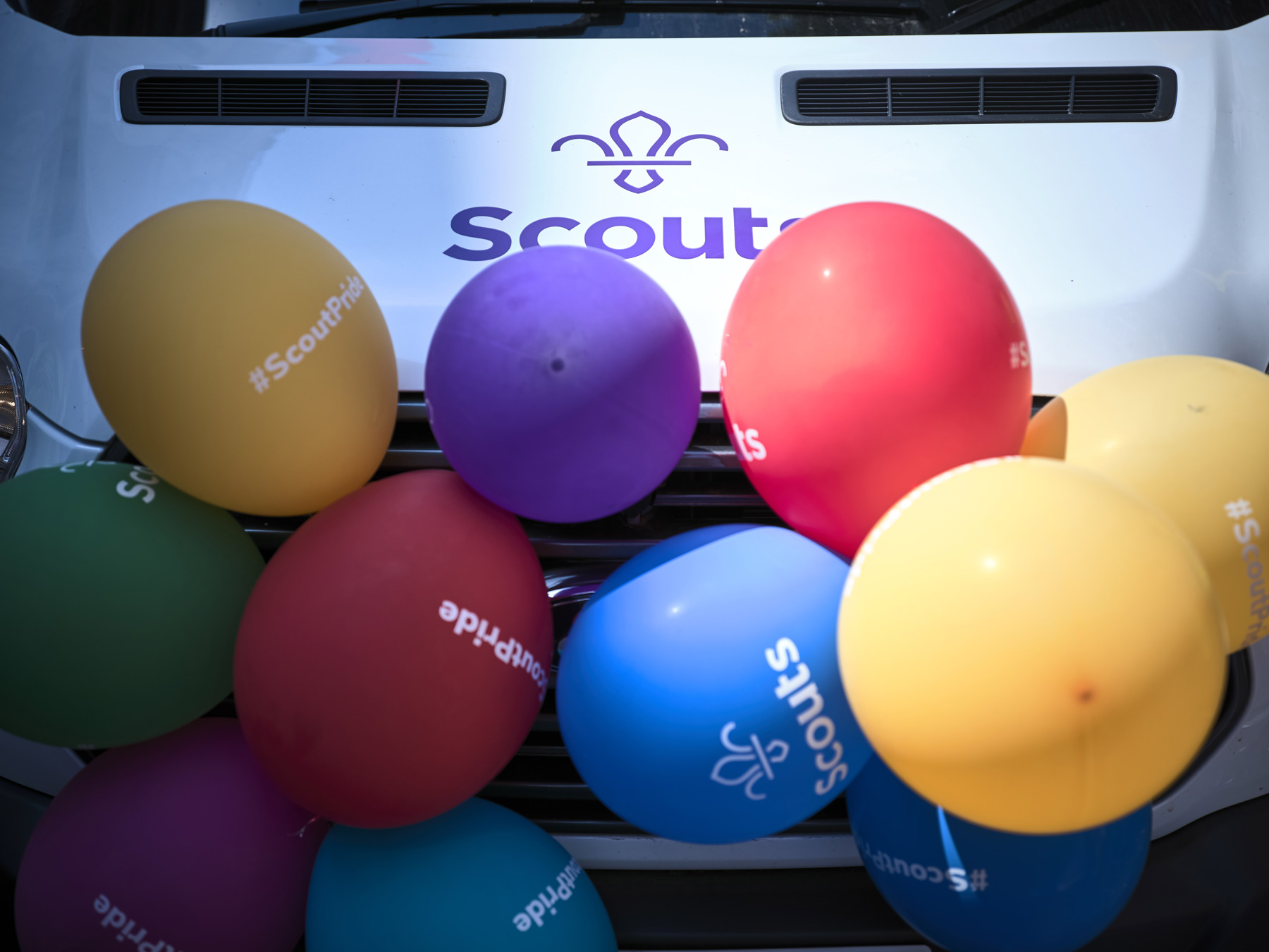 The front of a white Scouts minibus covered in multi-coloured balloons at London Pride