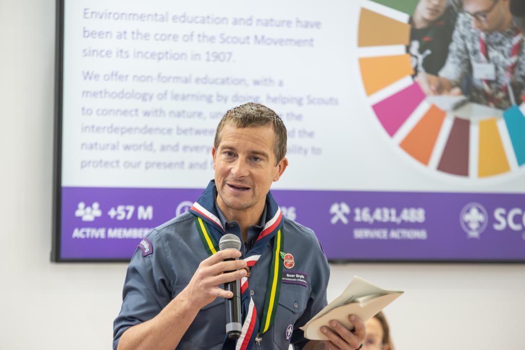 Bear Grylls holds a microphone and paper while giving a presentation at COP26