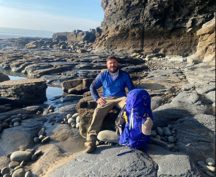 Chris the coast walker wearing a blue top sitting on rocks