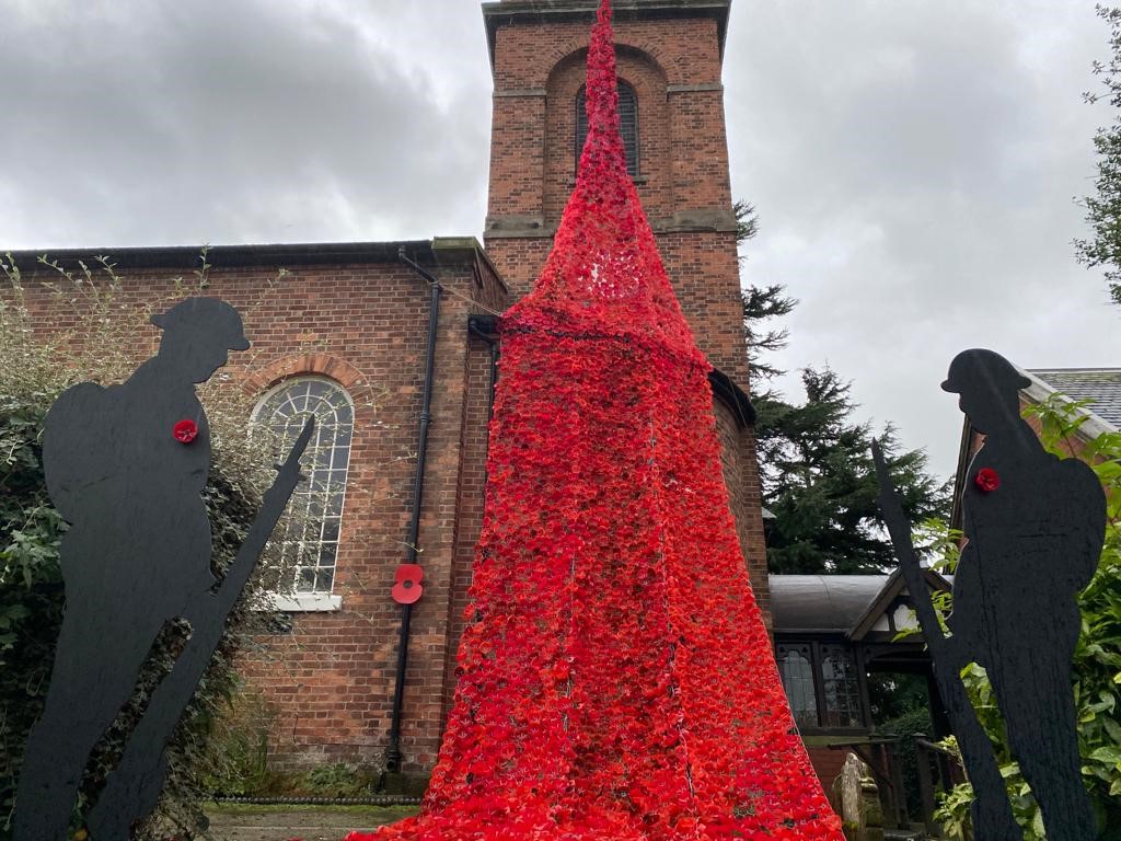 A large poppy display with the silhouettes of two soldiers outside a church