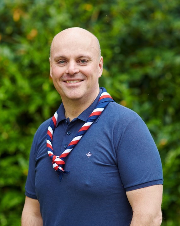 Carl Hankinson smiling at the camera while wearing a navy Scouts polo shirt and stripy scarf