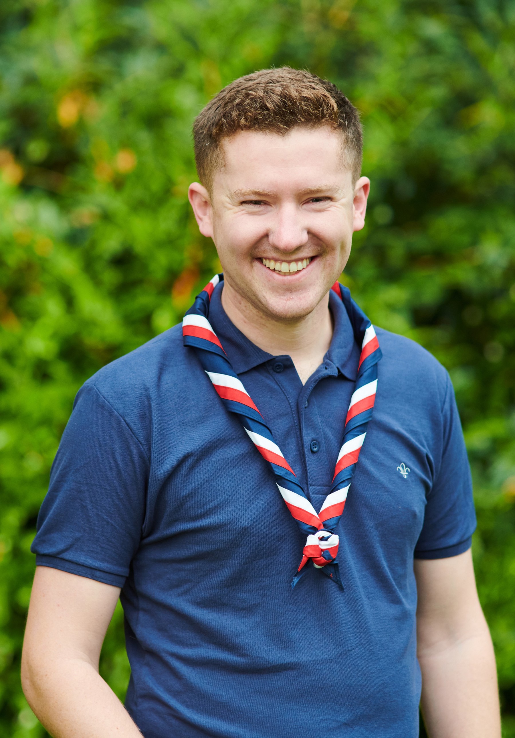 Ollie Wood smiling at the camera while wearing a navy Scouts polo shirt and stripy scarf