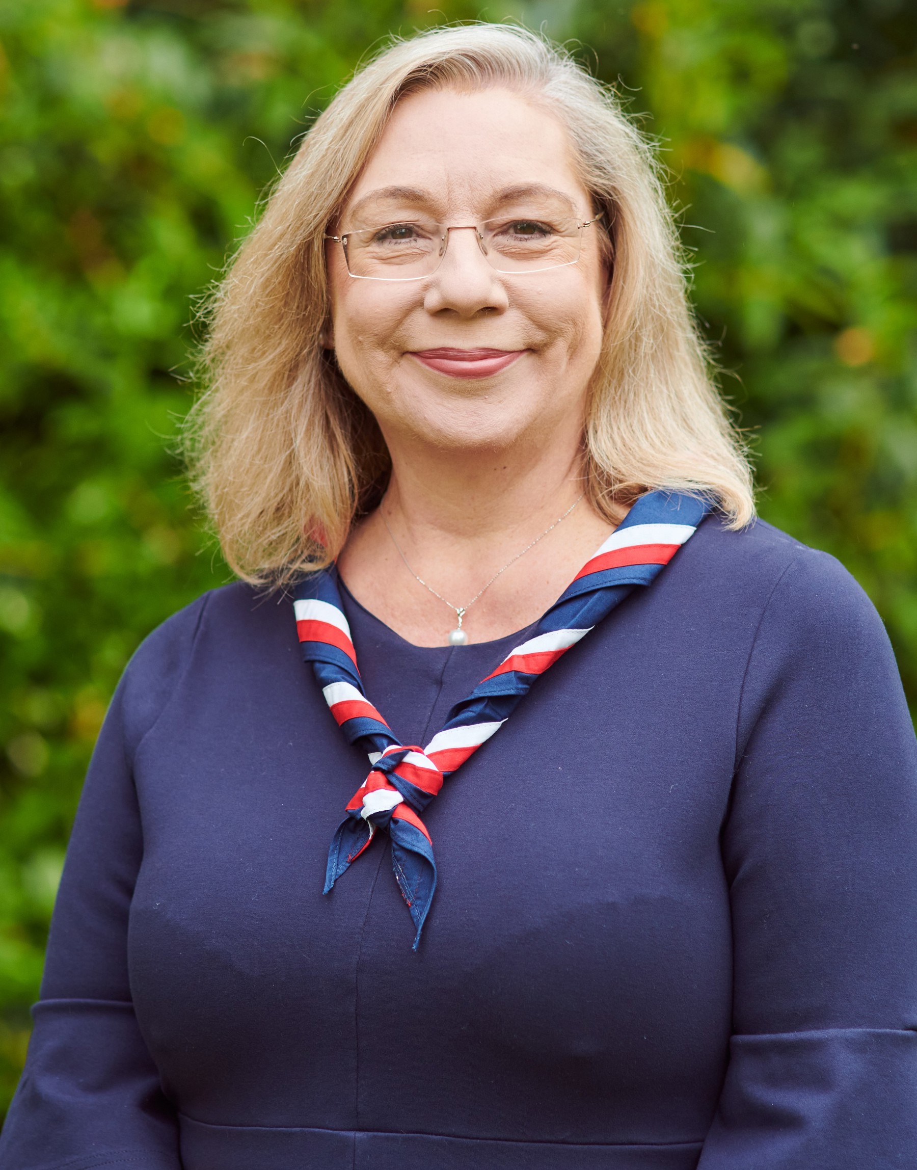 Jennie Price smiling at the camera wearing glasses and a navy top and stripy scarf