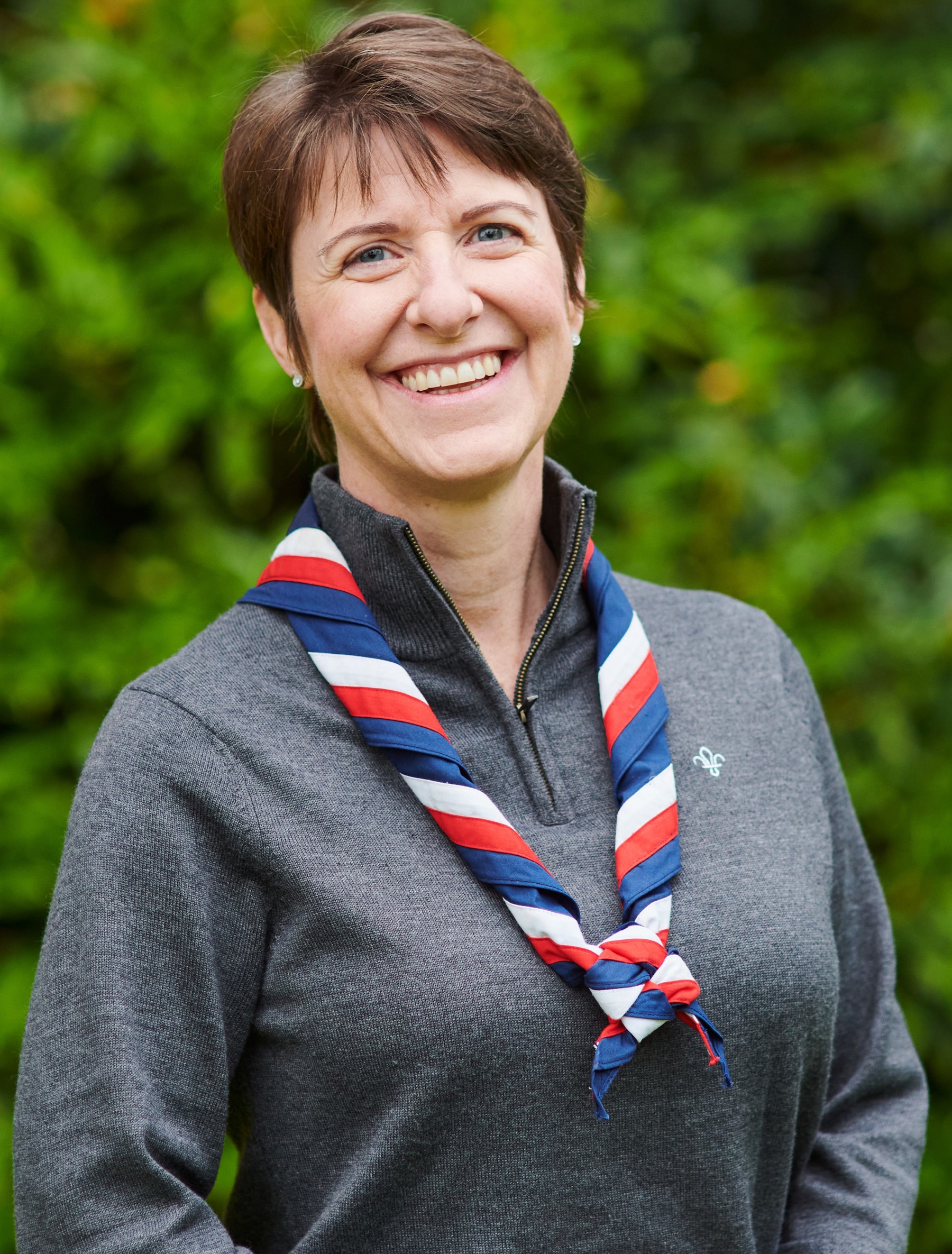 Caroline Pearce smiling at the camera while wearing a grey Scouts jumper and stripy scarf