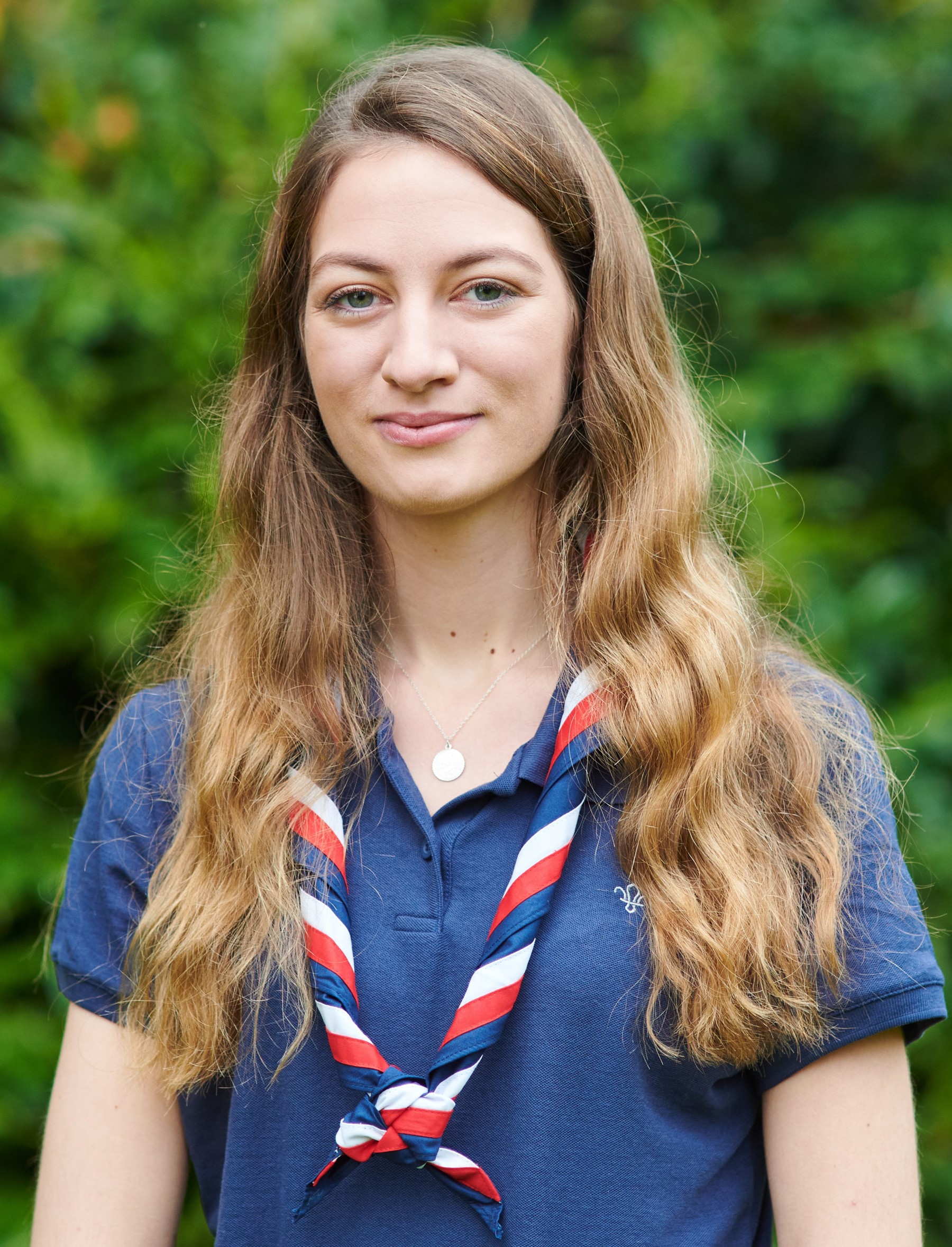 Rhiannon Wells smiling at the camera while wearing a navy Scouts polo shirt and stripy scarf