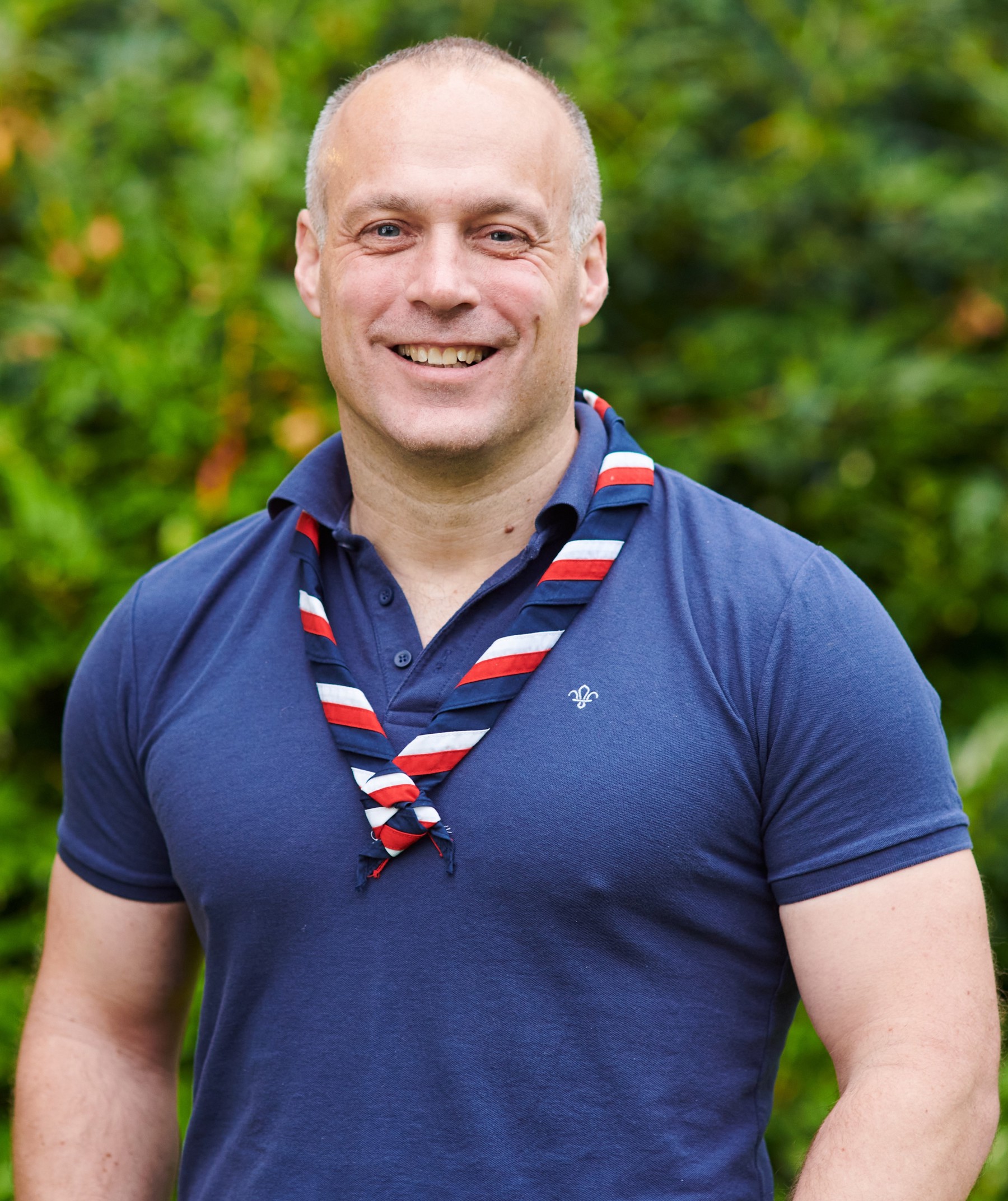 Michael Wood-Williams smiling at the camera while wearing a navy Scouts polo shirt and stripy scarf