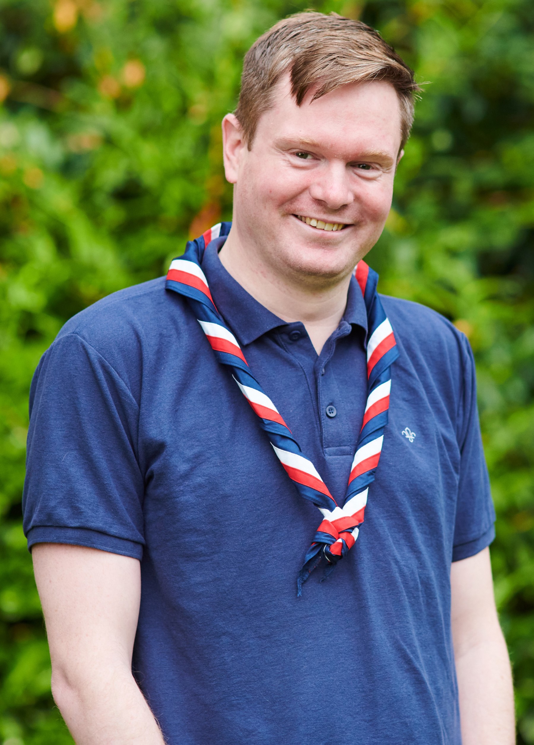 Craig Dewar-Willox smiling at the camera while wearing a navy Scouts polo shirt and stripy scarf