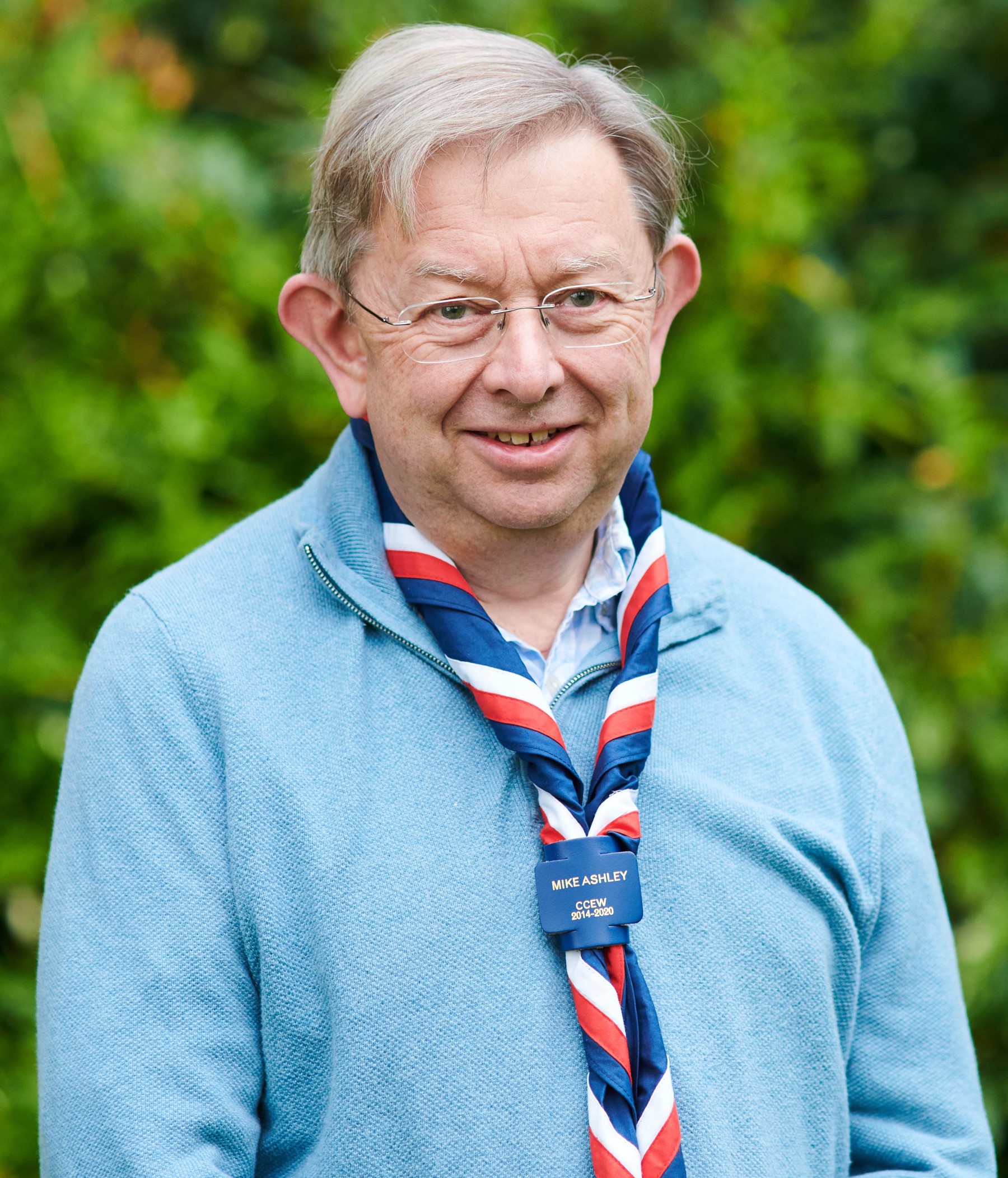 Mike Ashley smiling at the camera wearing glasses, a light blue jumper and stripy scarf