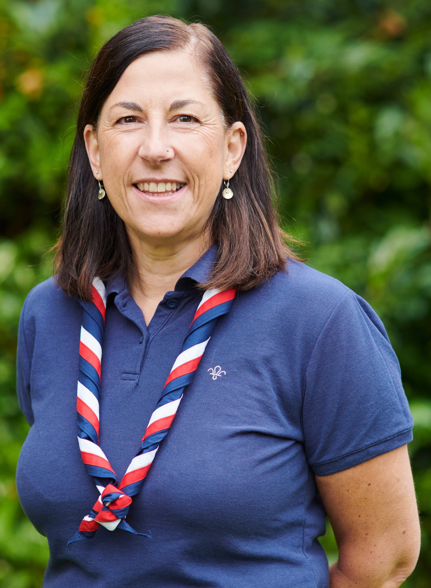 Liz Walker smiling at the camera wearing a navy Scouts polo shirt and stripy scarf