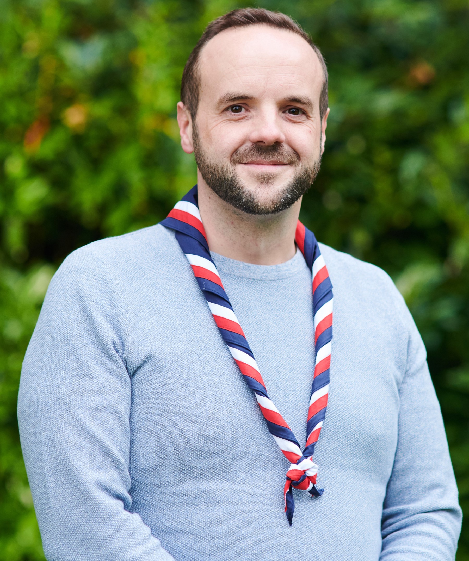 Peter Oliver smiling at the camera while wearing a long-sleeved light blue top and stripy scarf
