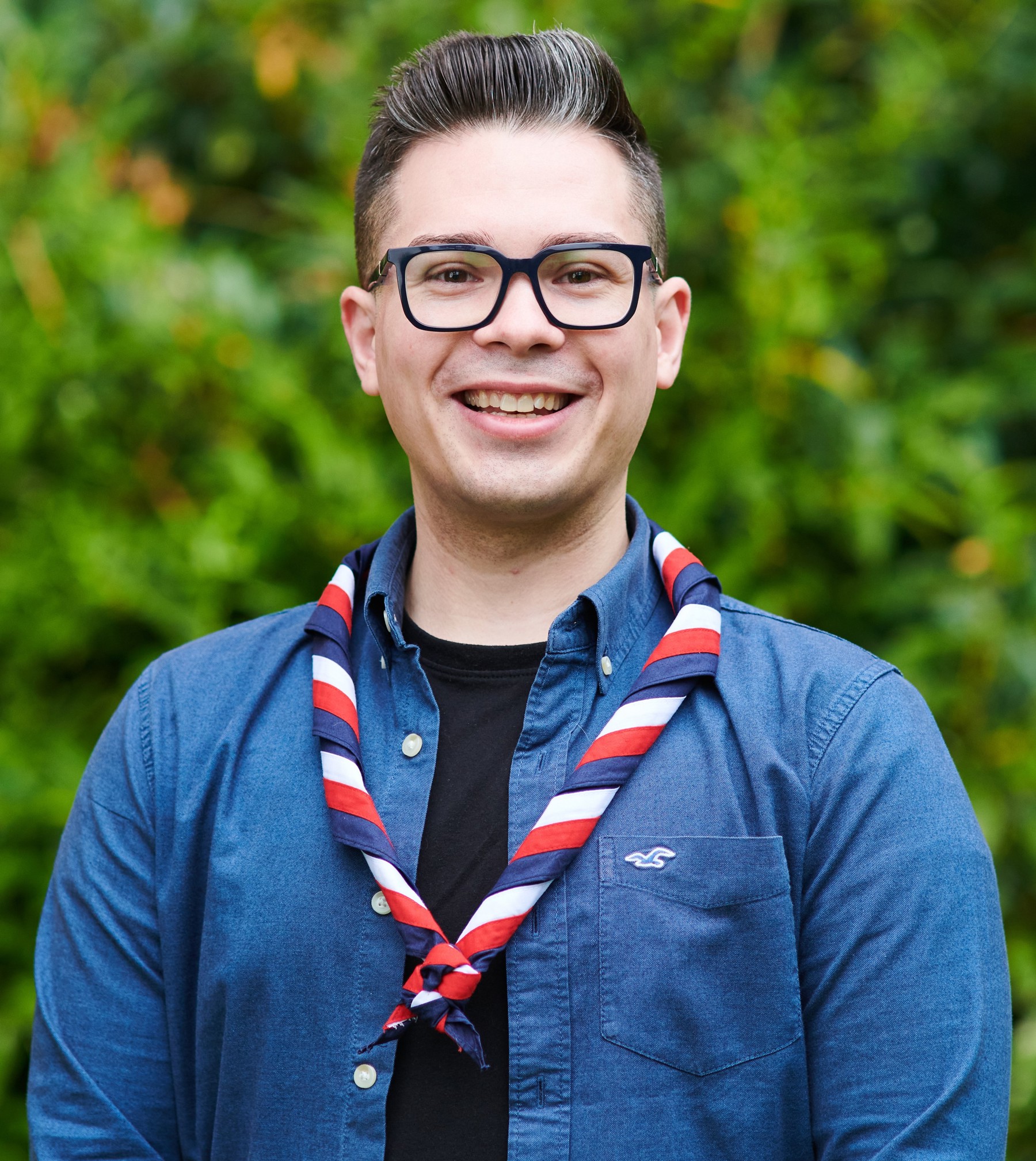 Jake Myatt smiling at the camera while wearing a black top, navy shirt and stripy scarf