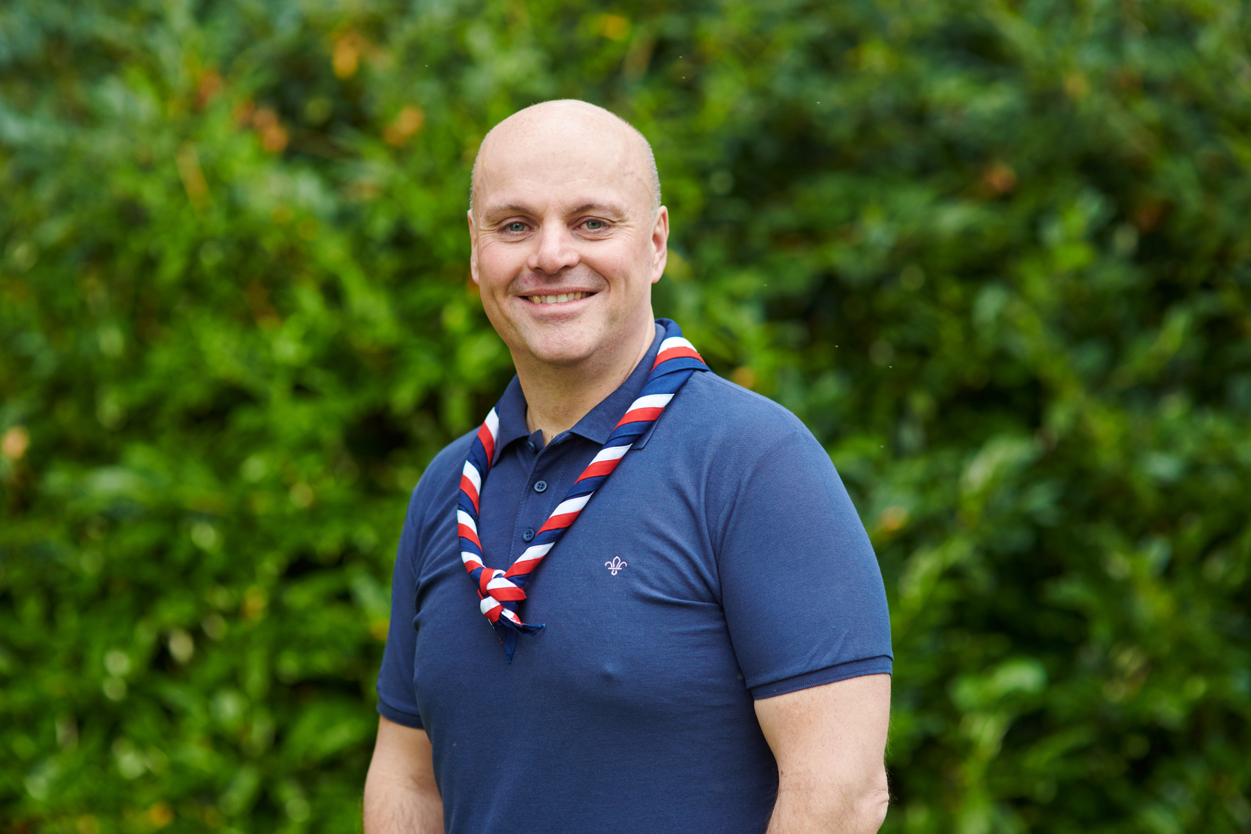 Carl Hankinson smiling at the camera while wearing a navy Scouts polo shirt and stripy scarf