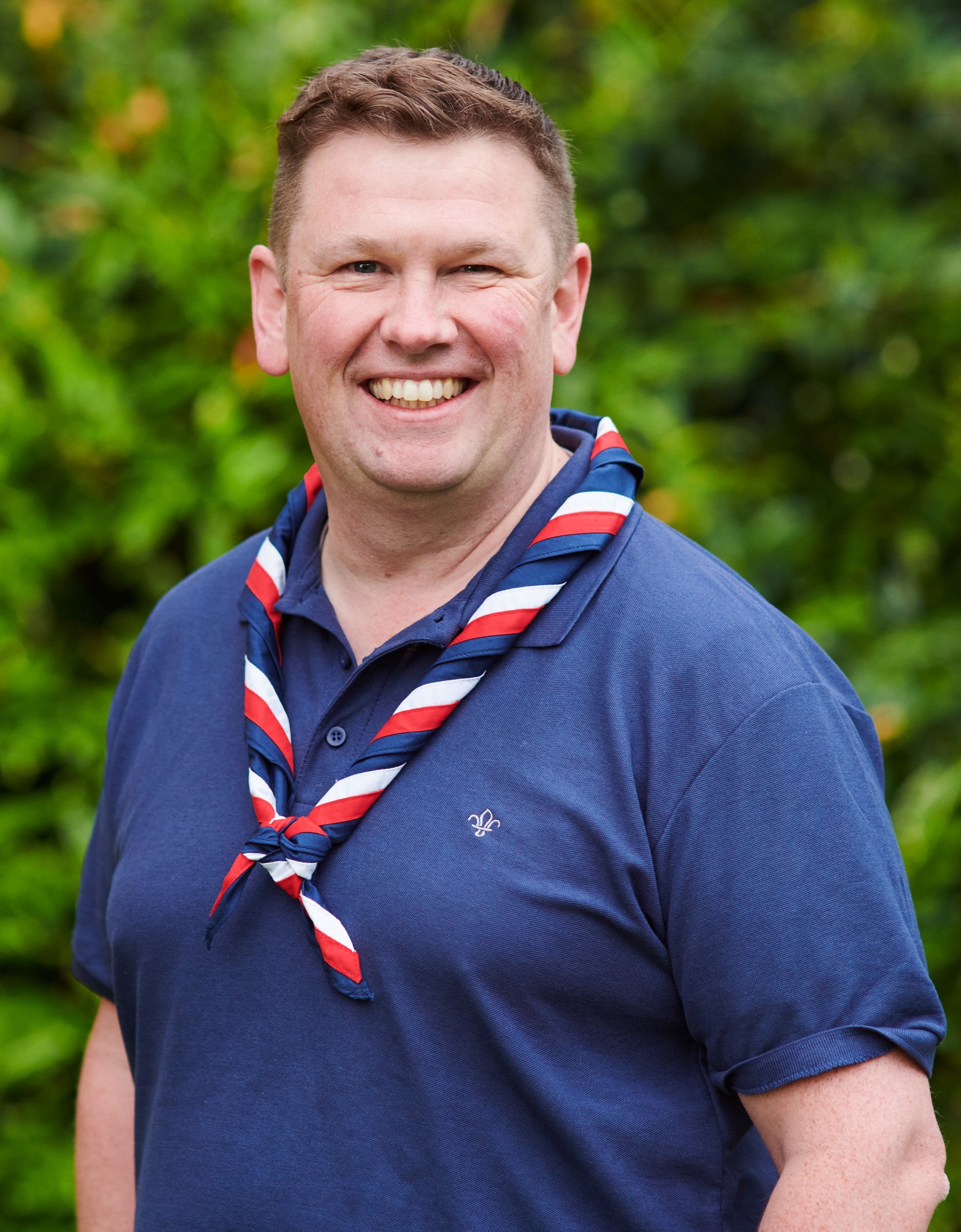 Craig Turpie smiling at the camera while wearing a navy Scouts polo shirt and stripy scarf