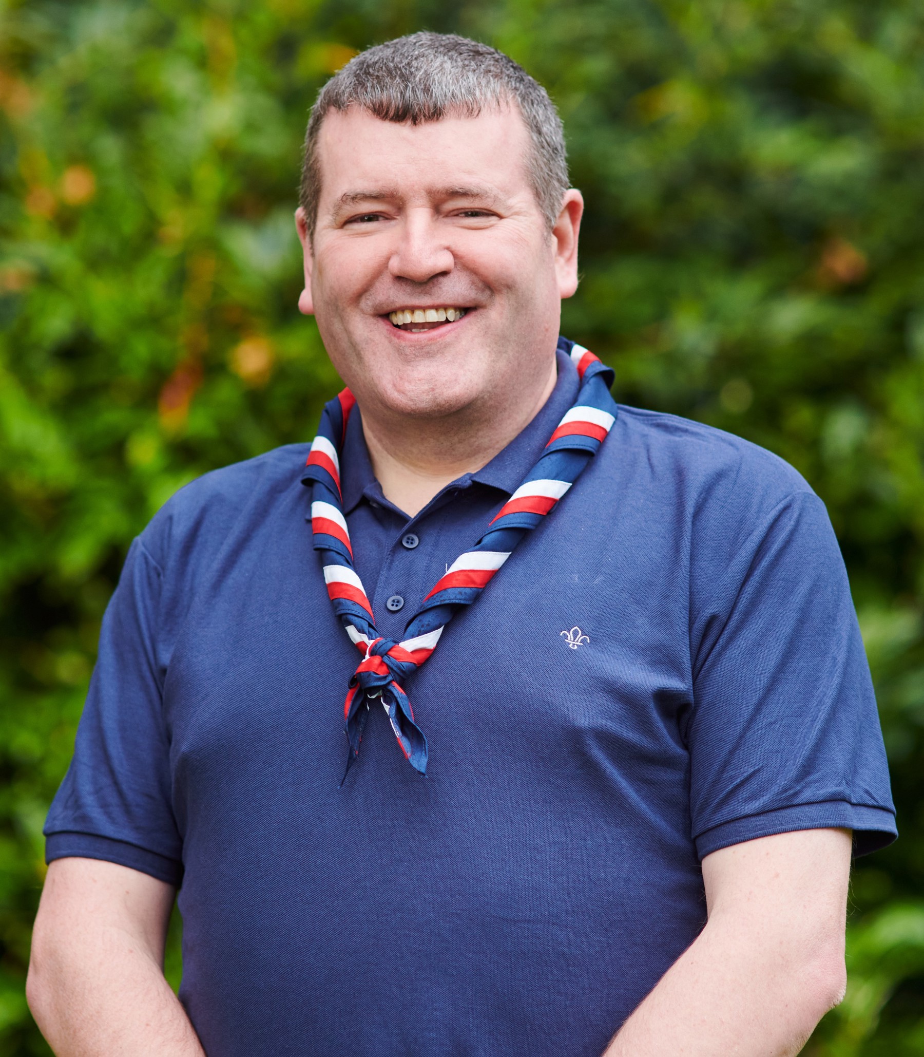 Andrew Sharkey smiling at the camera while wearing a navy Scouts polo shirt and stripy scarf