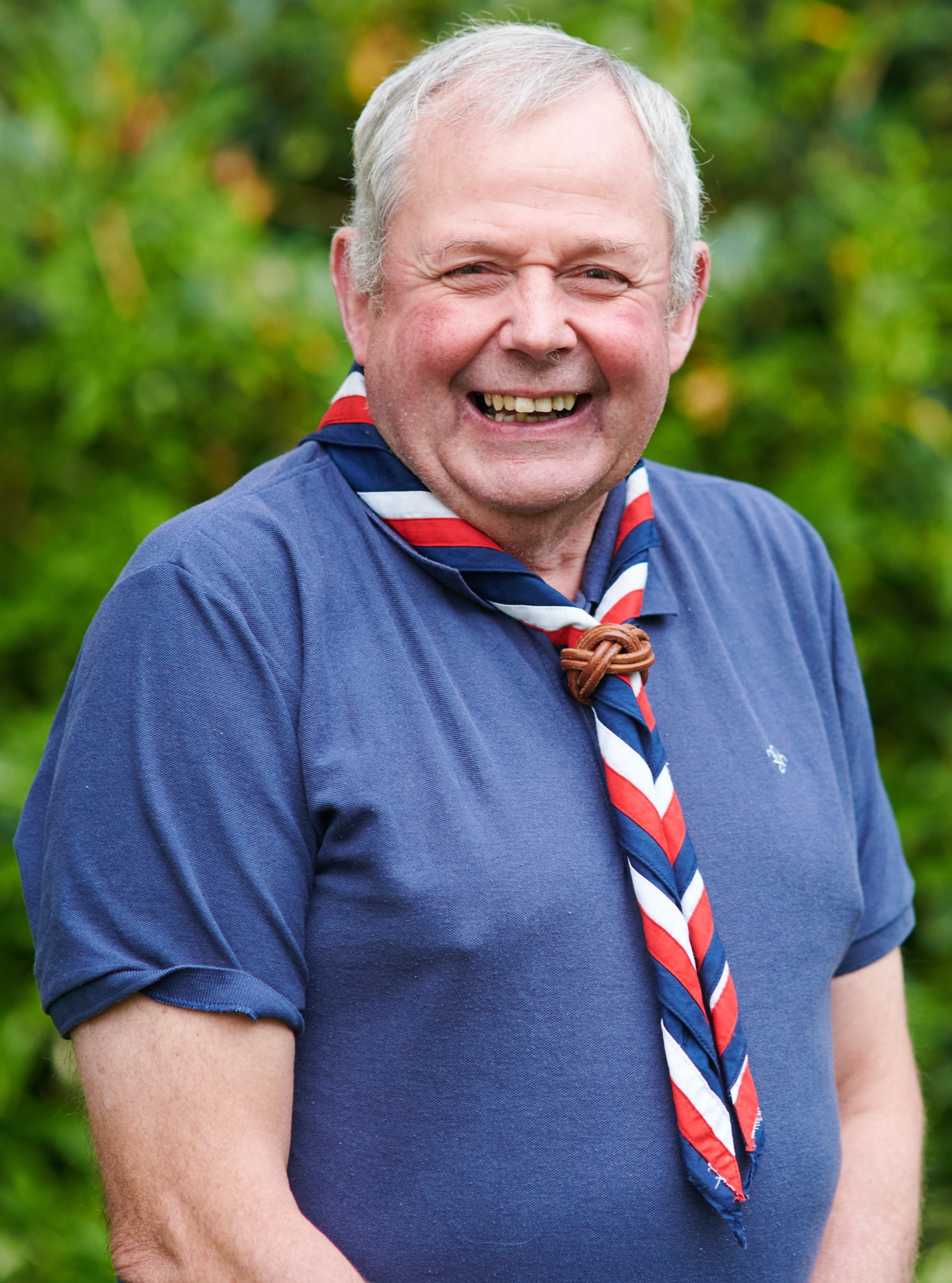 Stephen Donaldson smiling at the camera while wearing a navy Scouts polo shirt and stripy scarf
