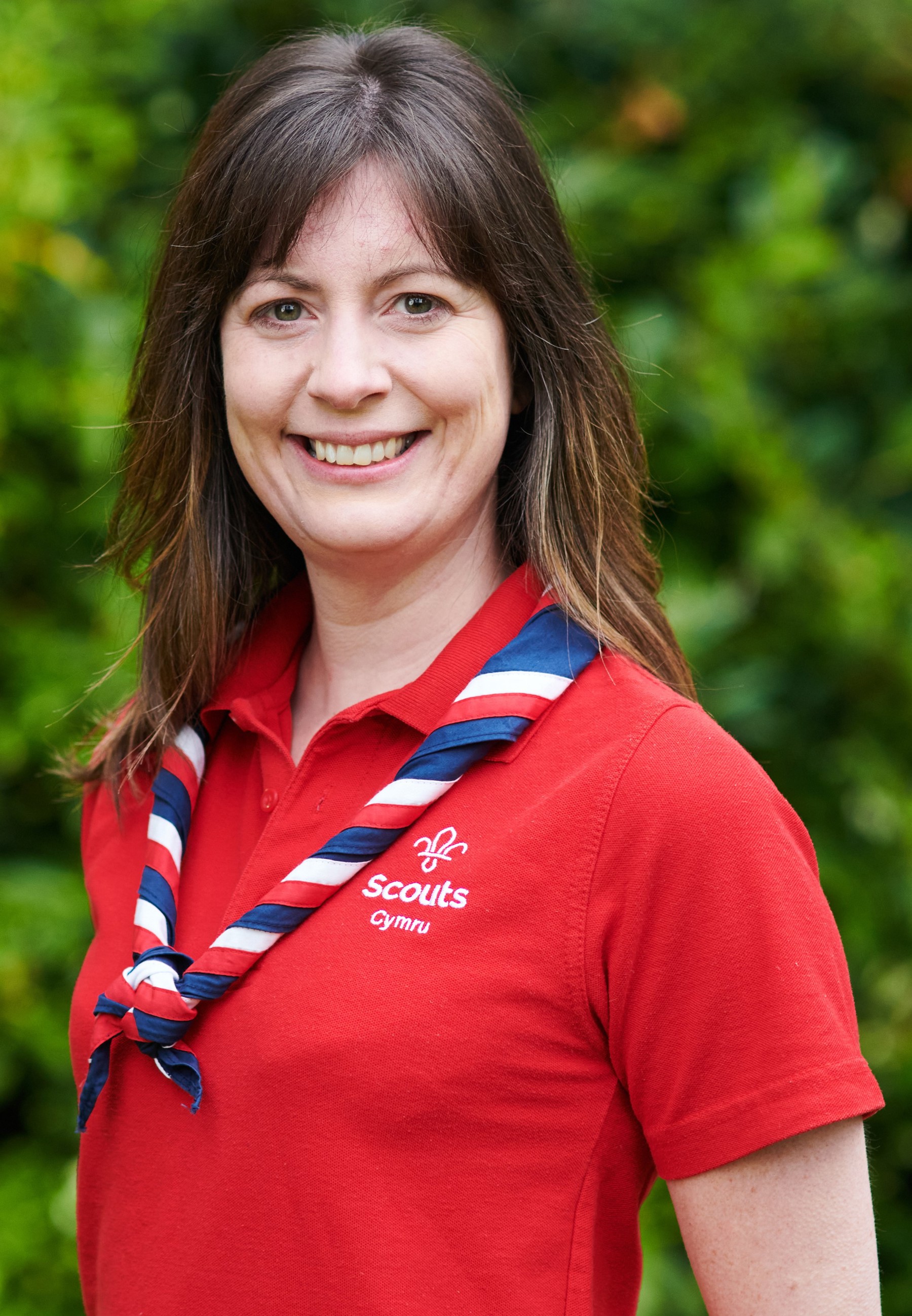 Rhian Moore smiling at the camera while wearing a red Scouts polo shirt and stripy scarf