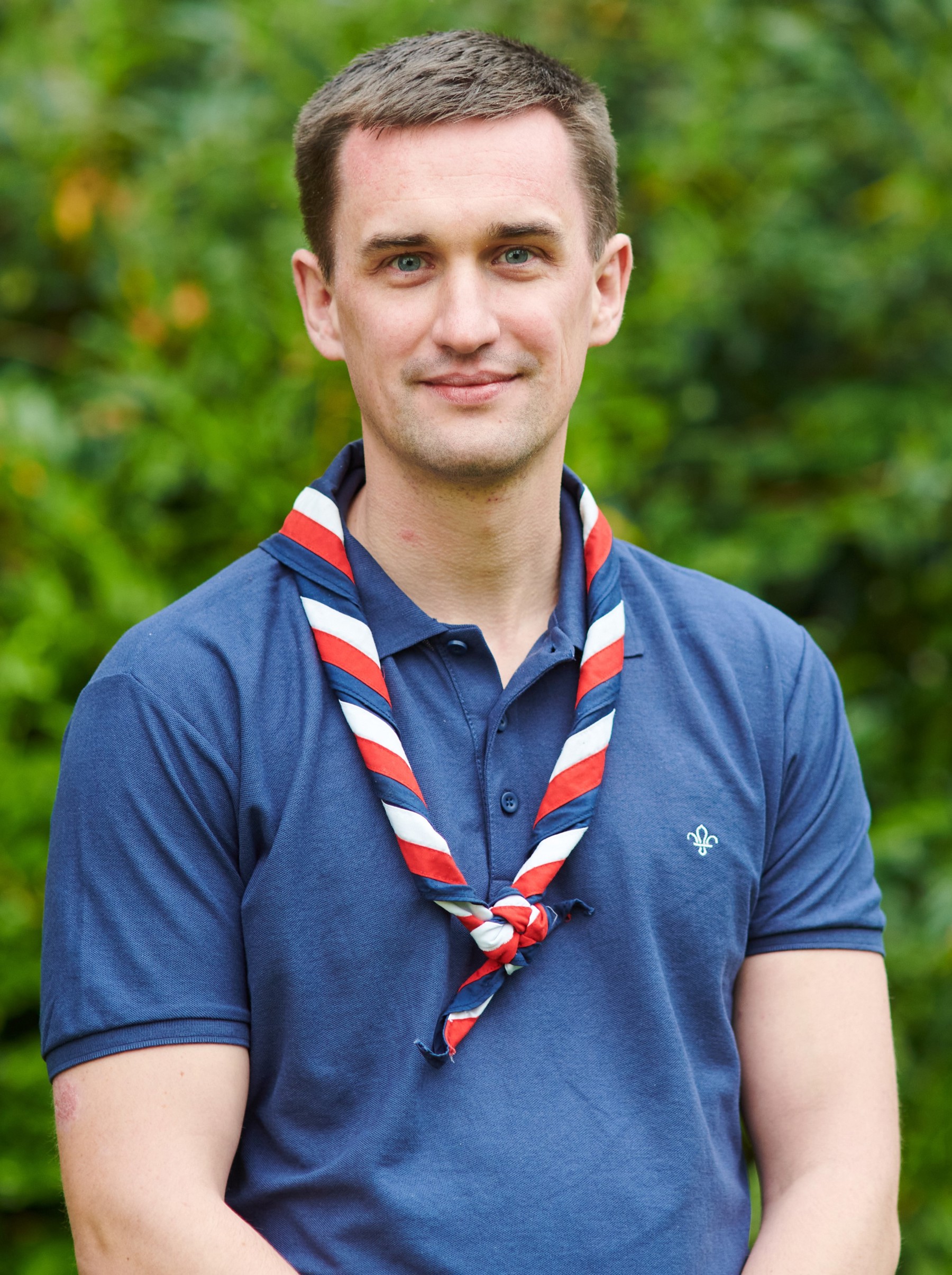 Callum Kaye smiling at the camera while wearing a navy Scouts polo shirt and stripy scarf