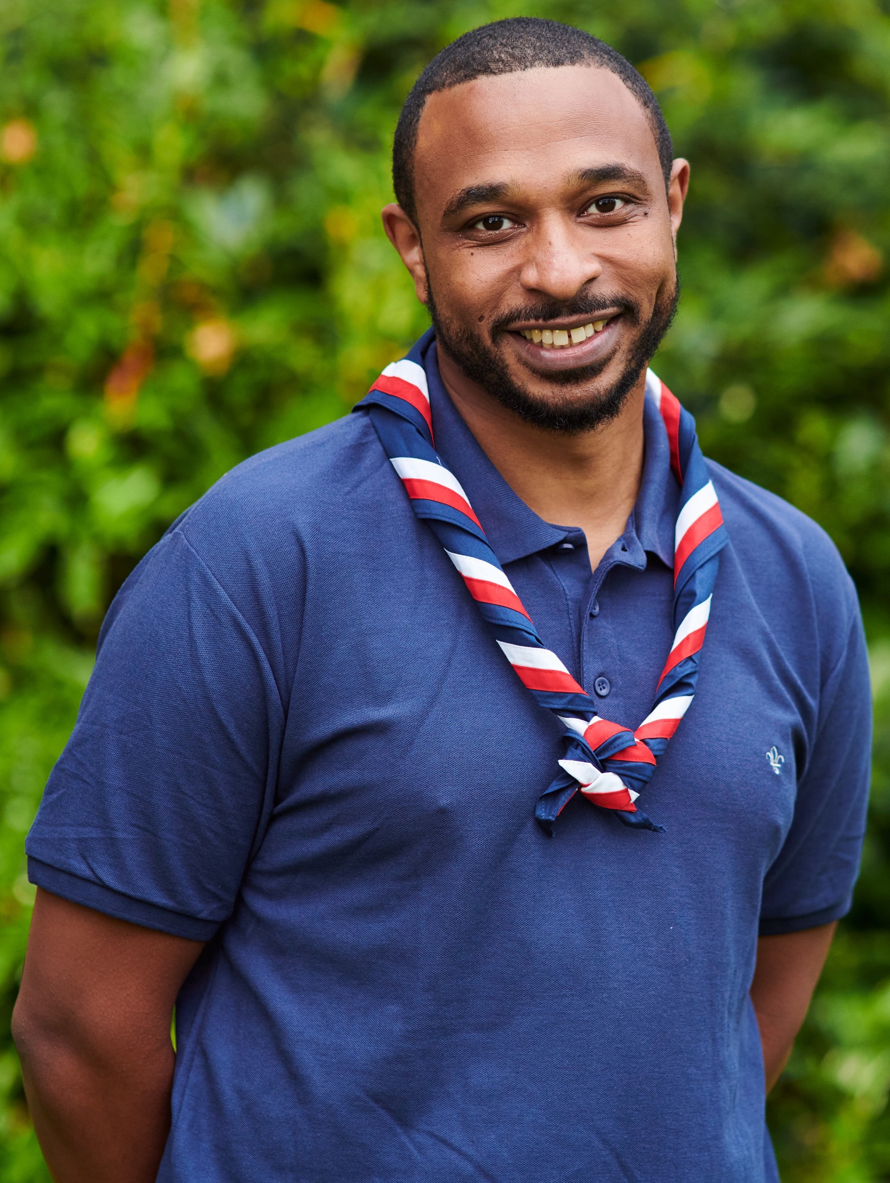Yousif Eltom smiling at the camera while wearing a navy Scouts polo shirt and stripy scarf