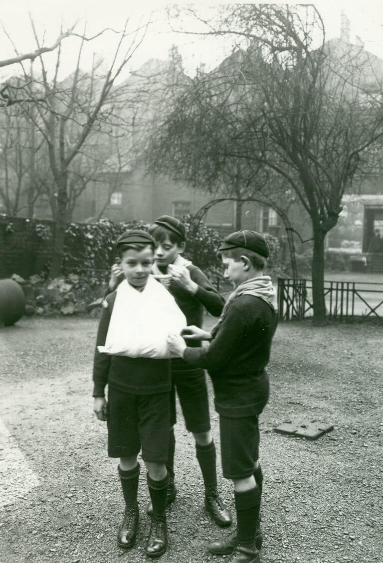 Black and white photo of a Cub demonstrating first aid skills by putting another Cub's arm in a sling