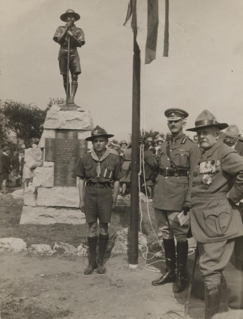 Image the memorial , which is a Scout in uniform standing on a plinth. Two uniformed Scouts and soldier are also in the picture.