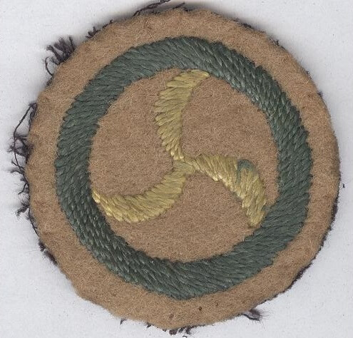 Image shows the Missioner’s Badge, a green circle on a brown canvas with a golden wheel in the centre
