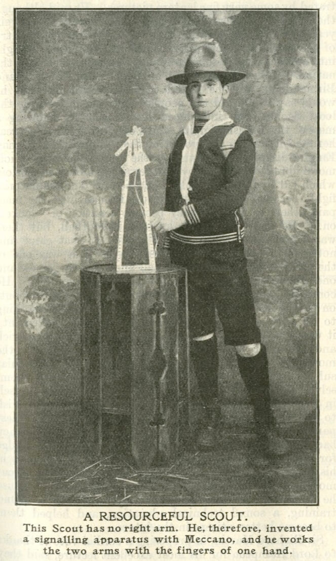 Black and white photo of a Scout in uniform posing with a triangular device. The caption below reads 'A resourceful Scout. This Scout has no right arm. He, therefore, invented a signalling apparatus with Meccano, and he works the two arms with the fingers of one hand.'