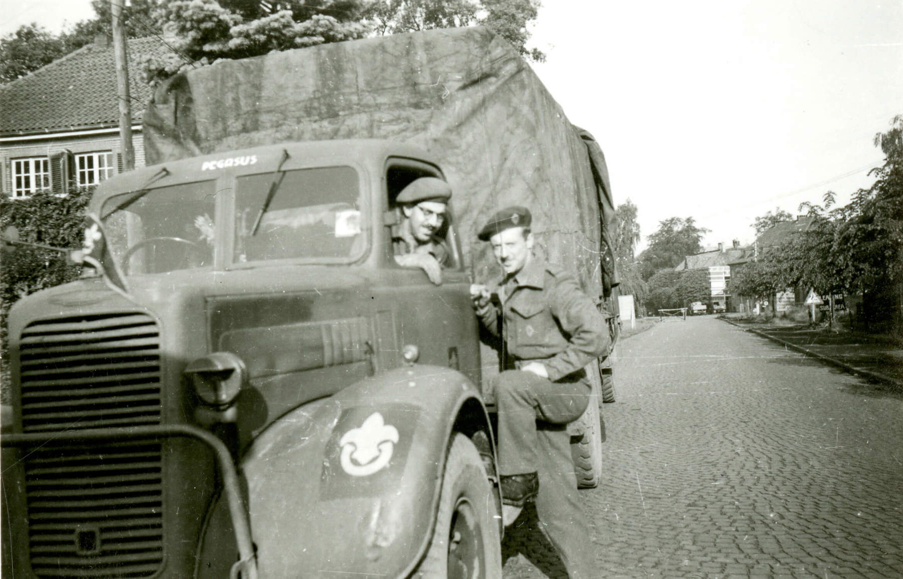 Black and white photo of two men posing next to an Army truck featuring the Scouts emblem