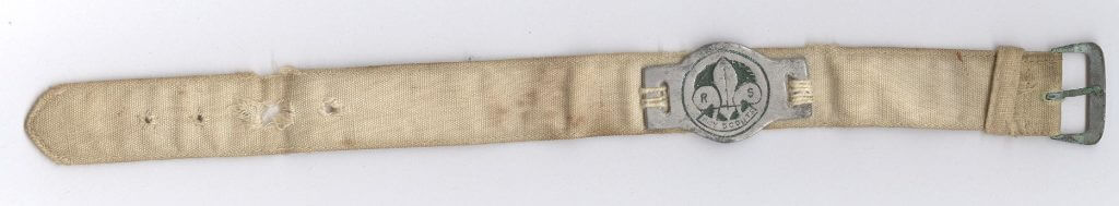 An off-white canvas wristband with a metal Scouts emblem and metal fastening