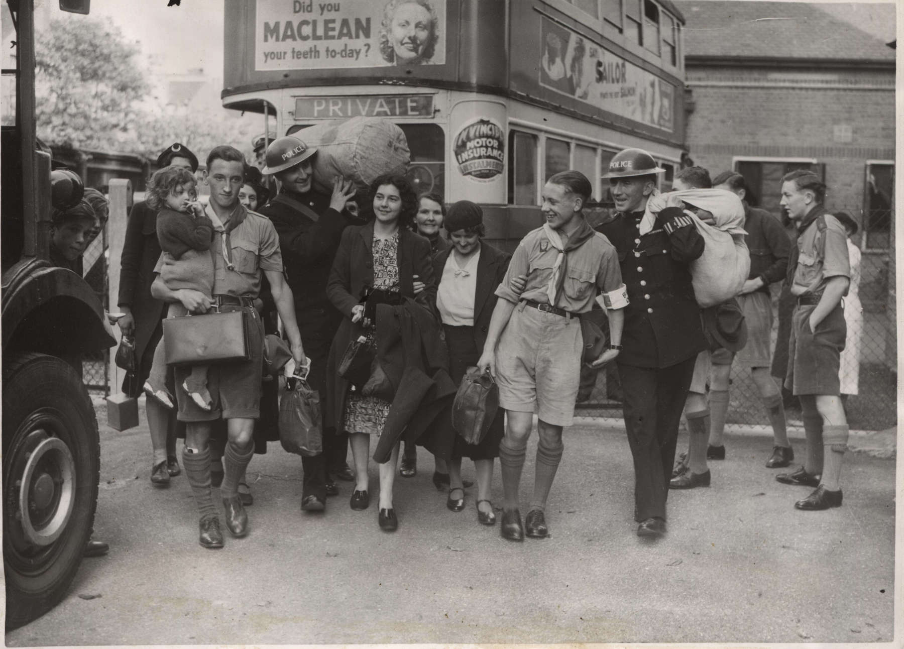 Black and white photo of a group of Scouts helping to carry children and luggage