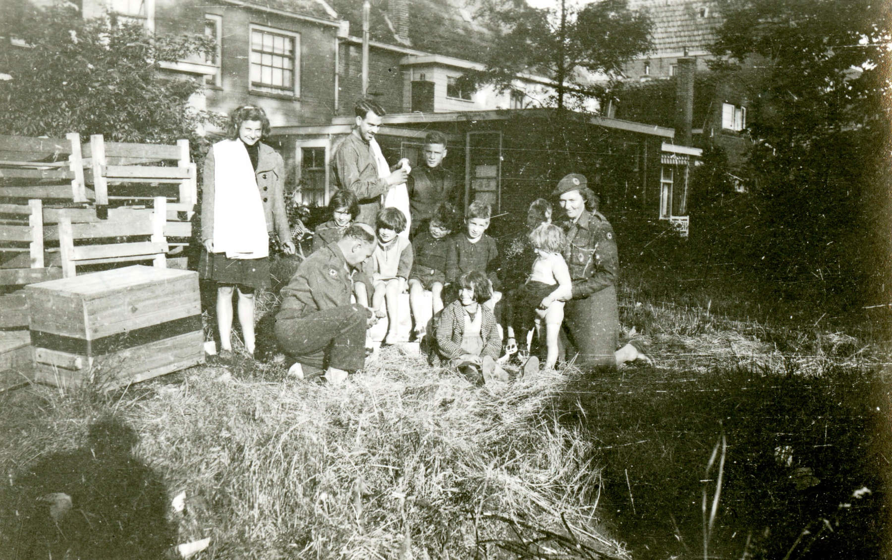 Black and white photo of Scouts kneeling on the grass in a garden as they help to fit a family with clothes