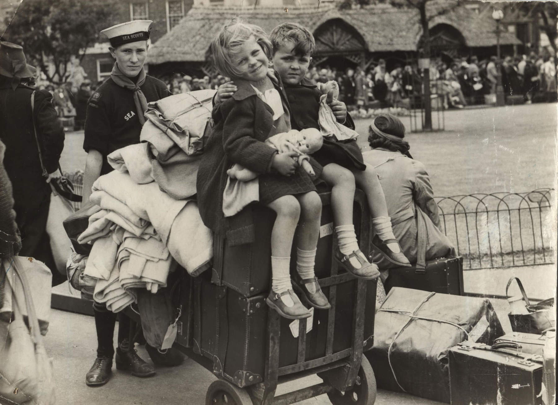 Black and white photo of two young people posing with their arms around each other while sitting on top of a cart pushed by a Scout