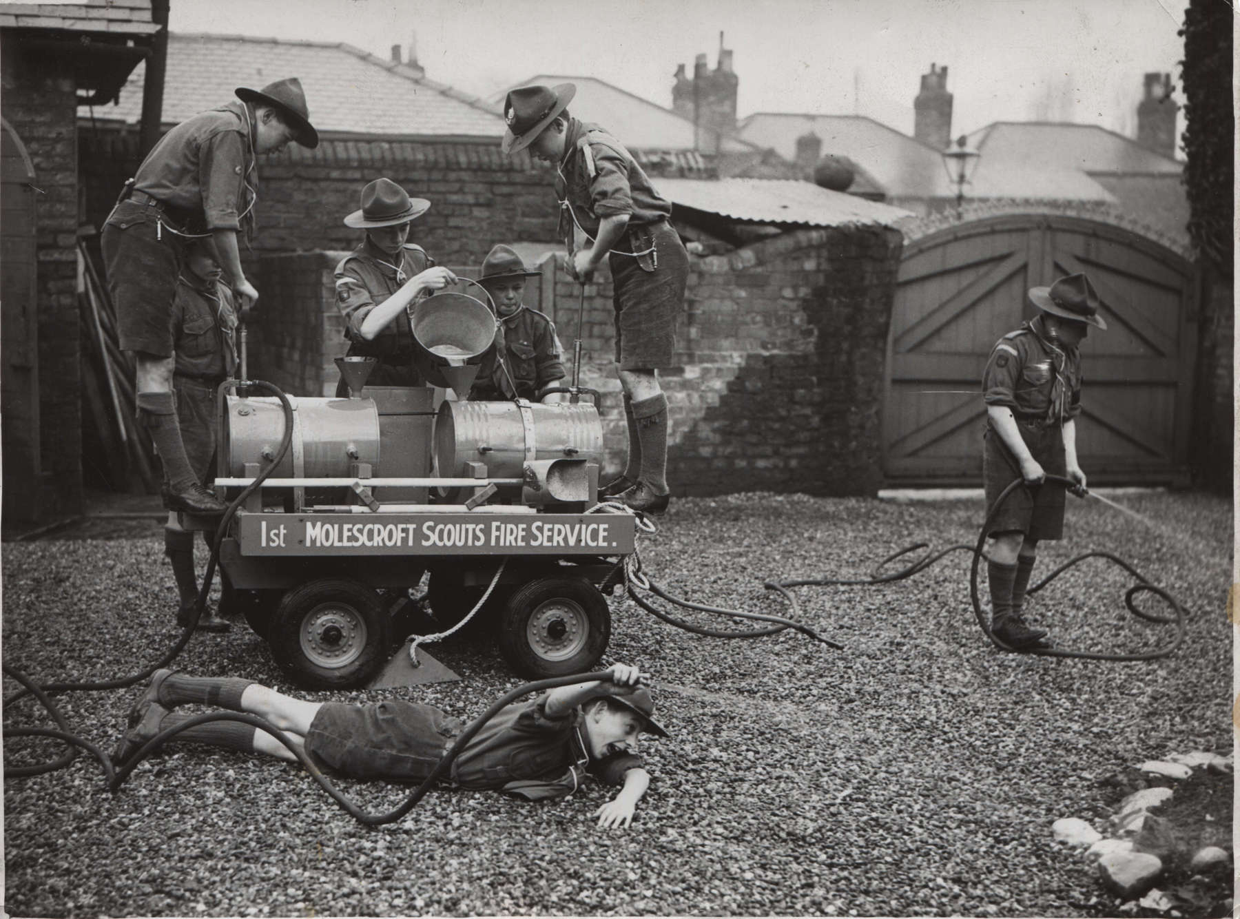 Black and white photo of a group of Scout pumping water and holding hoses