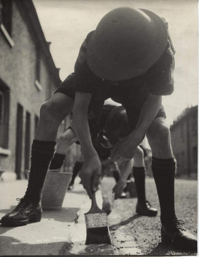 Black and white photo of a line of Scouts painting white lines on the side of the road