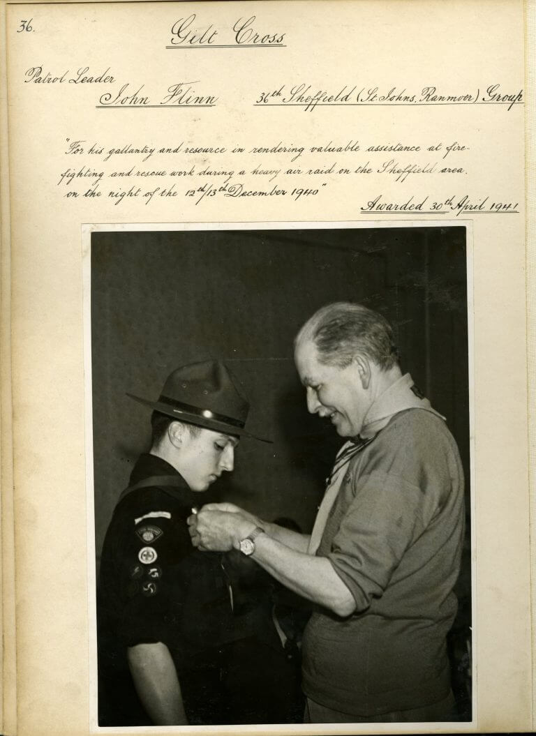 Certificate with a black and white picture of John Flinn having a medal pinned on to his shirt by an older man.