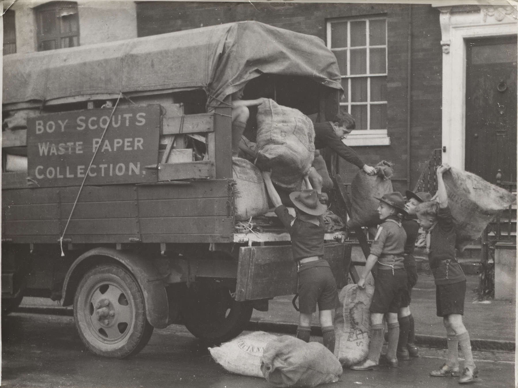 Black and white photo of Scouts loading packages into the back of a truck that has 'Boy Scouts Waste Paper Collection' written on the side