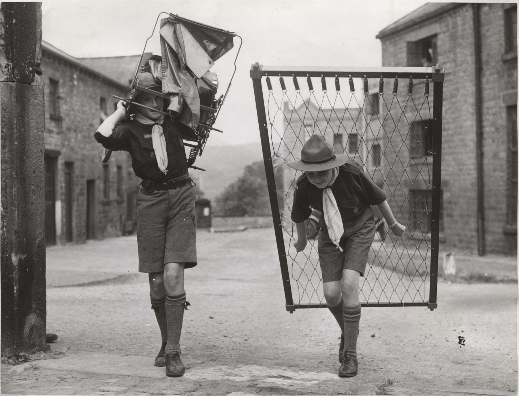 Black and white photo of two Scouts walking down the street while carrying two large pieces of scrap metal