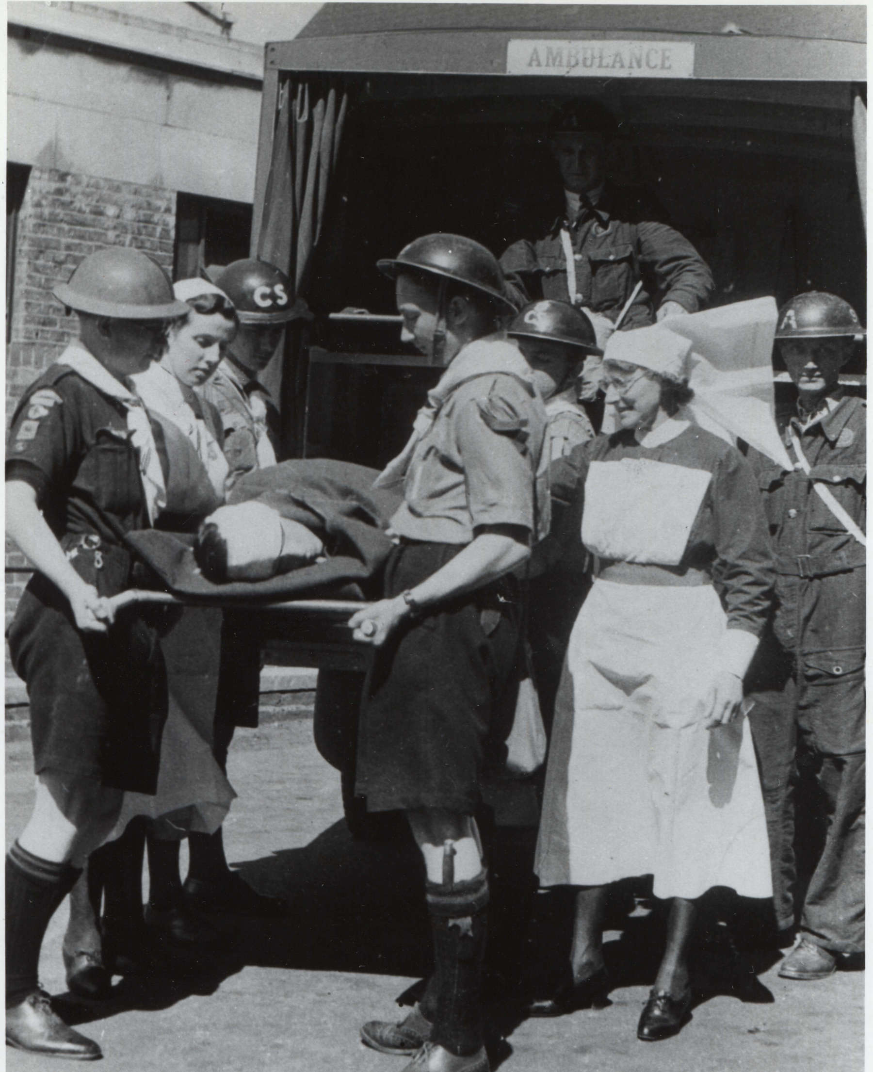 Black and white photo of a group of Scouts carrying a hospital stretcher out of the back of an ambulance