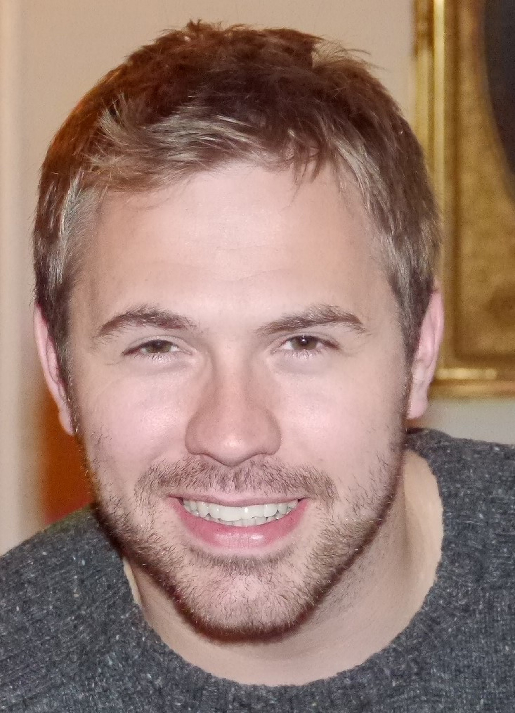 Liam Burns smiling at the camera while wearing a grey jumper