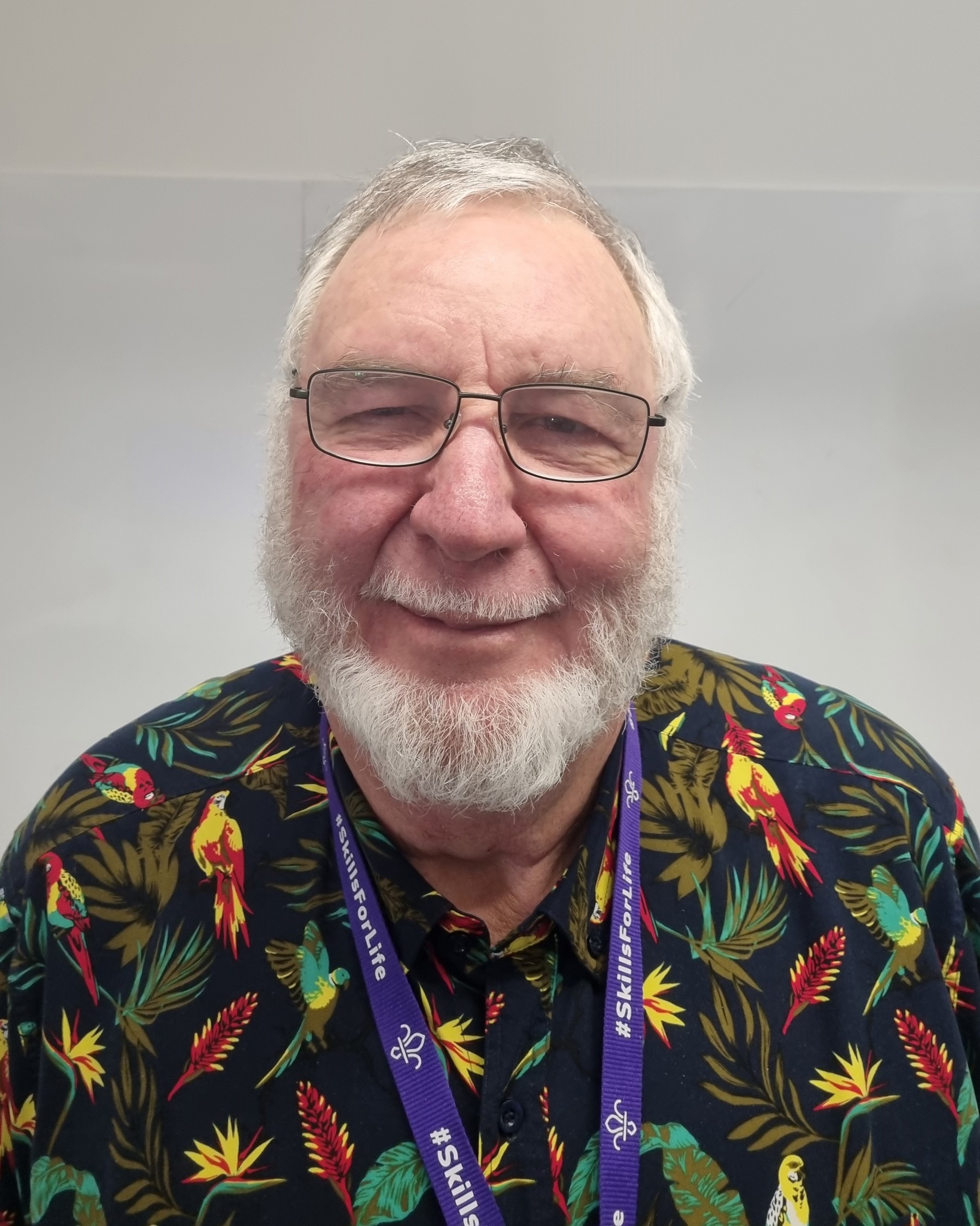 Dirk Grobler smiles at the camera wearing shirt with bright prints of birds and leaves, and a purple Scout lanyard