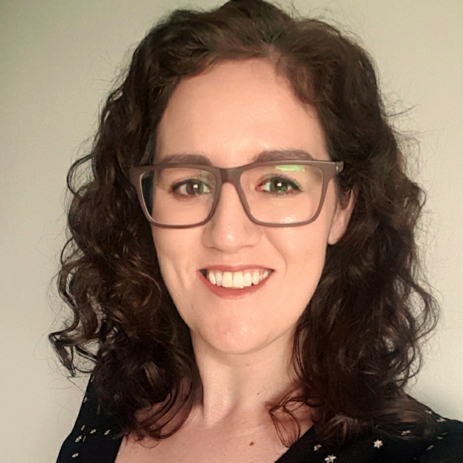 Joanna Gregson smiles at the camera wearing glasses and black top with silver stars on