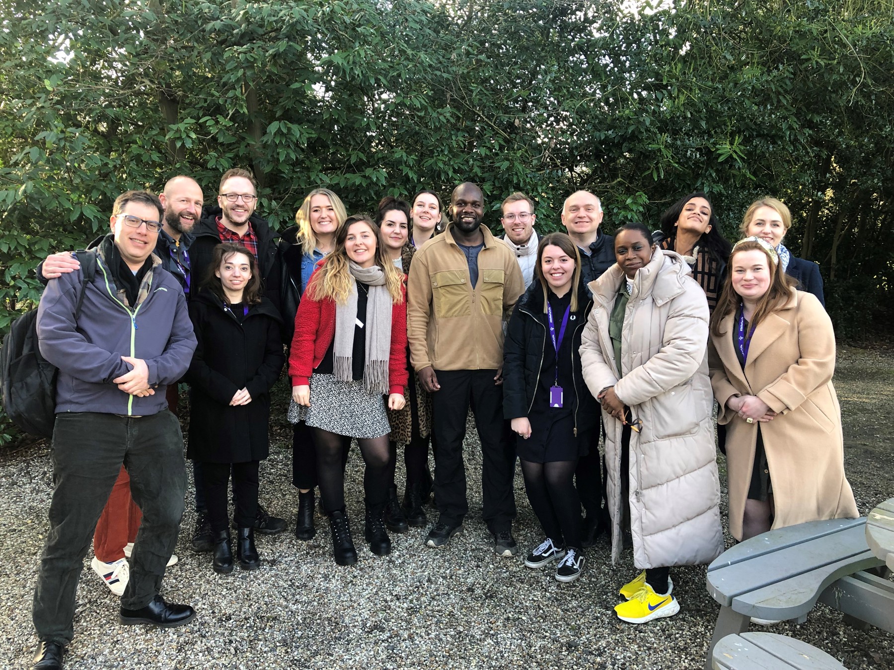 Group shot outdoors of the Communications team with Dwayne Fields in the centre with trees behind