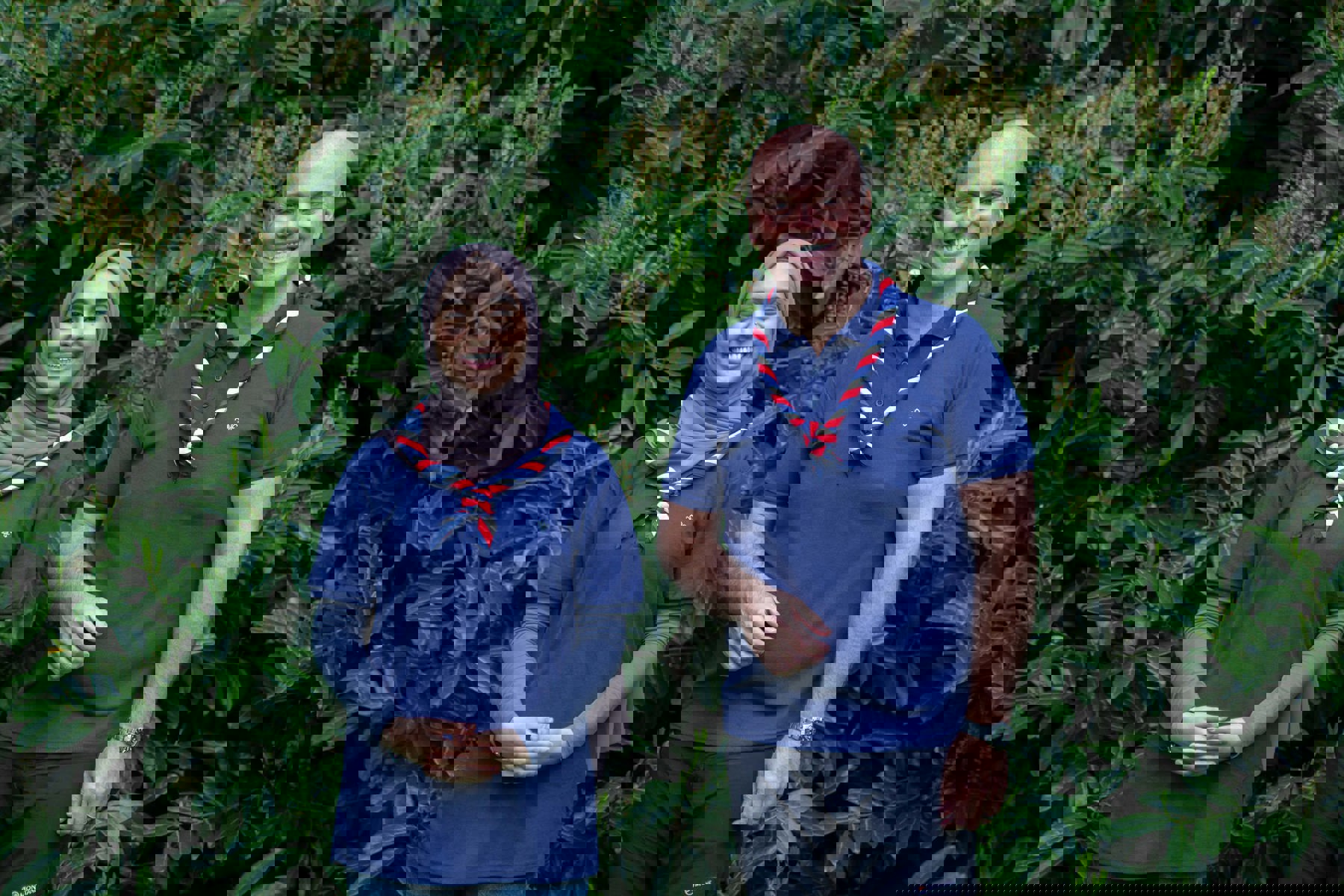 Ayesha and Carl wearing Scouts polo shirts and neckers, standing in front of bushes, smiling at the camera