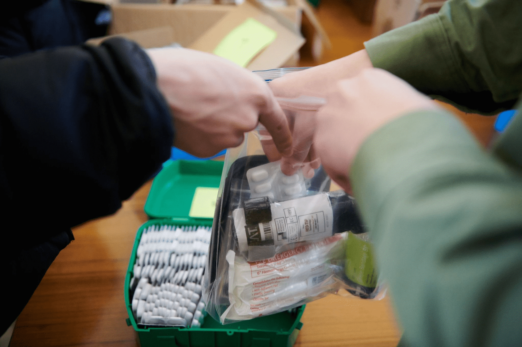 Two pairs of hands are helping to put medicines and first aid equipment in a ziplock bag.