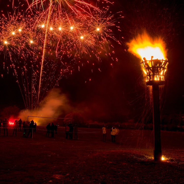 A beacon glowing alight with a golden flame, with golden fireworks in the background