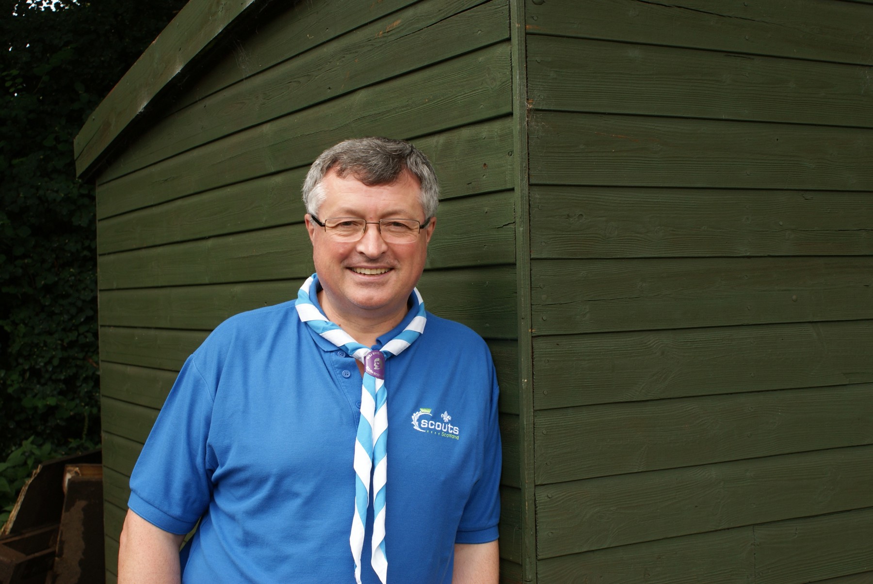An image of Graham Haddock OBE in a blue polo leaning up against a shed