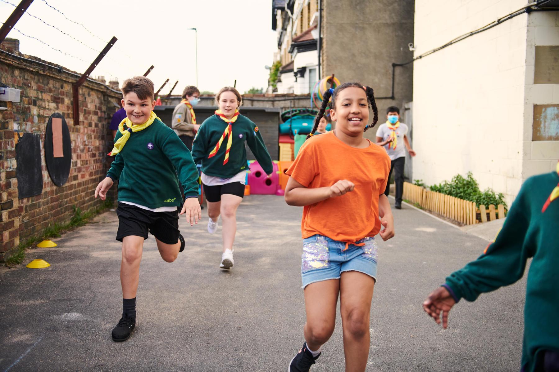 Three Cubs, two in uniform and one in an orange t-shirt, smile and run down the street